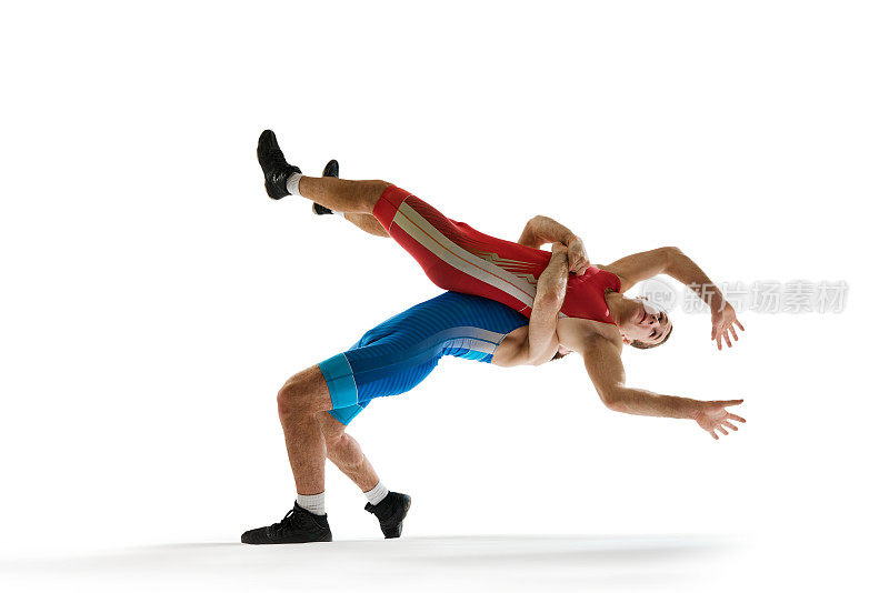 One wrestler in red uniform thrown by opponent in blue, both captured mid-fall in motion against white studio background.